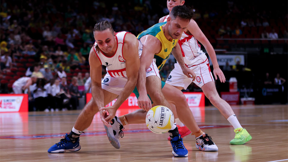 A photograph of two male netball players reaching down for the ball