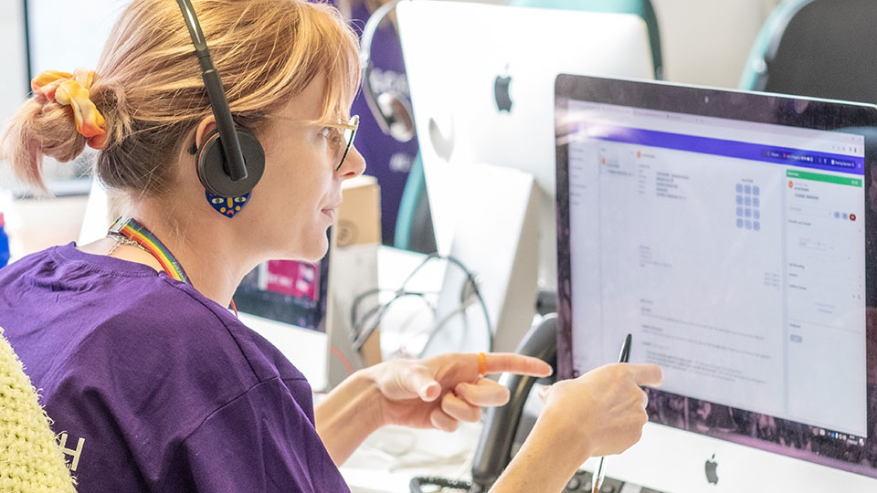 A call handler talking to a student on the phones using a telephones headset on results day, while looking at a computer screen
