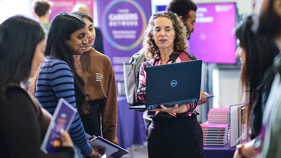 A careers adviser holding a laptop computer talking to a group of students