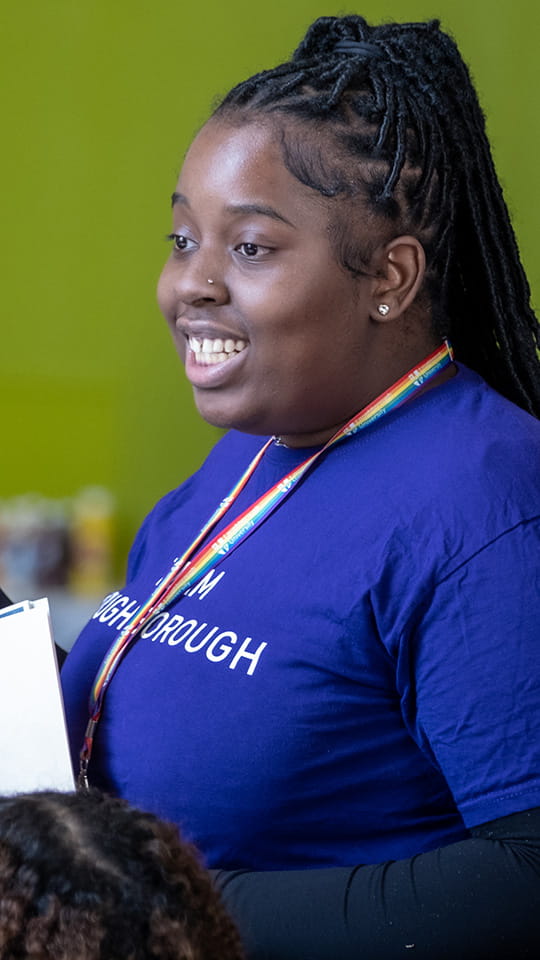 Sharon Oyeneye wearing a purple tee-shirt and rainbow lanyard talking to a group of children