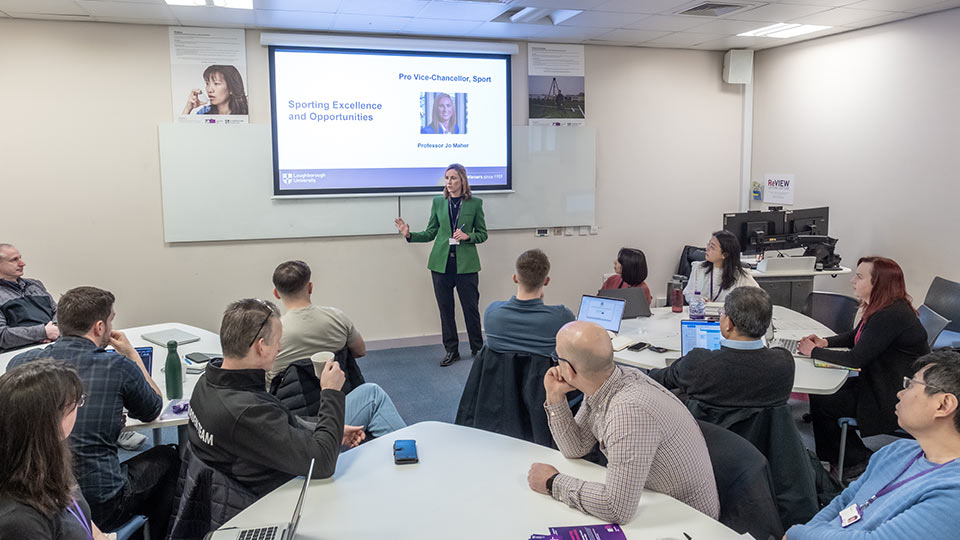 People sat at tables with one person standing presenting in front of a screen