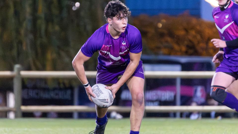 A male student playing rugby mid-game with the ball in his hand