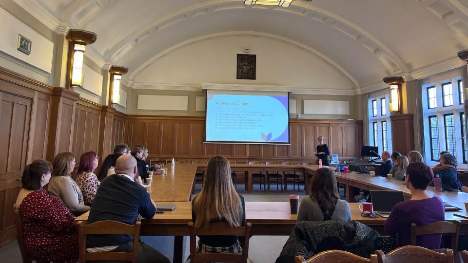 Group of colleagues sat in the Hazelrigg Council Chamber listening to someone presenting at the front of the room with the screen