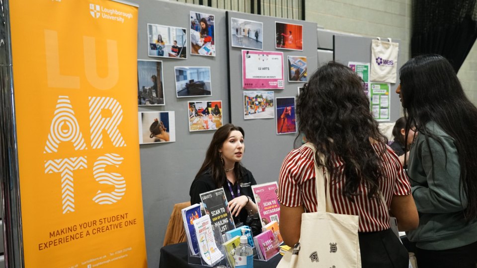 A girl sitting behind a desk at a stand talking to some customers