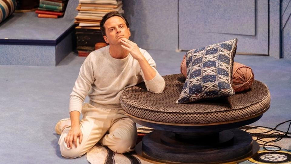 An actor sitting on the floor, resting his arm on a table, looking into the distance