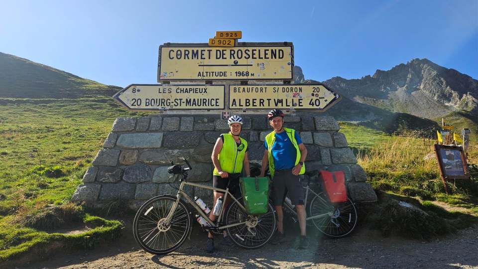 Richard and Ange standing with their bikes in front of a sign for Cormet de Roselend, a mountain pass in France.