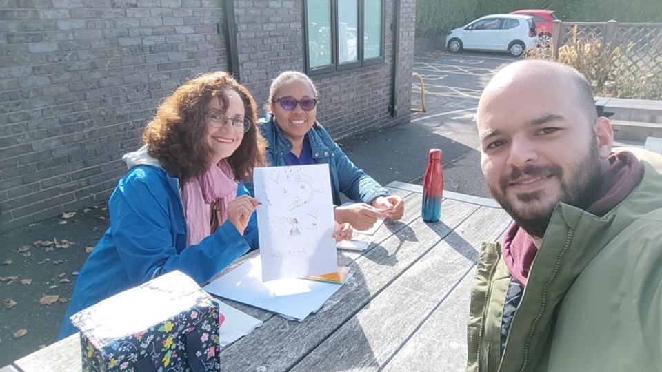 Three of the book club members sat together on an outside picnic bench smiling