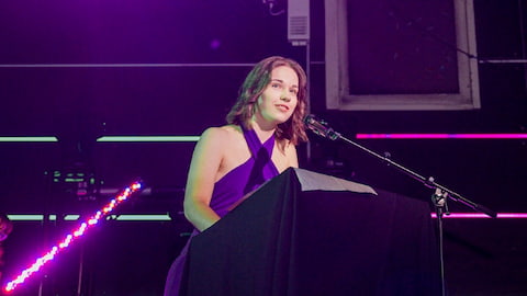 Daisy Newton standing on stage speaking into a microphones.