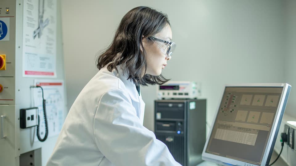 Student in lab coat and goggles looking at computer screen