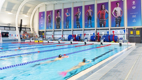 The Olympic-sized swimming pool at 麻豆視頻_麻豆直播_麻豆传媒官网. Swimmers are training in the pool. There are posters displayed of Team GB swimmers.