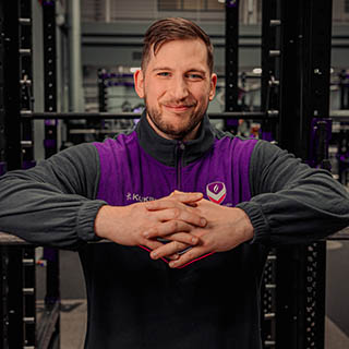 Jon is smiling for a headshot in the gym wearing Loughborough Sport kit.