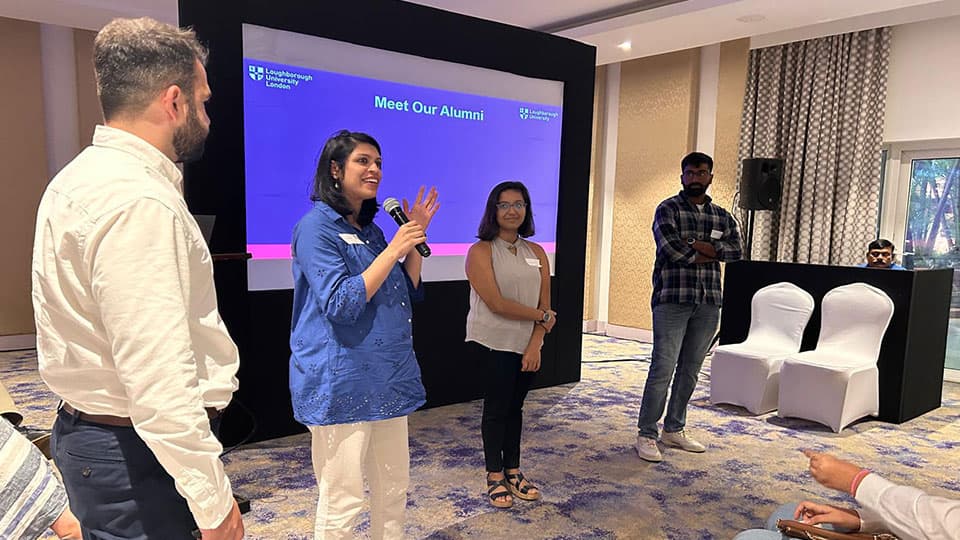A group of three alumni standing in front of a screen that says 'Meet our alumni' talking to an audience at 麻豆視頻_麻豆直播_麻豆传媒官网's India pre-departure event